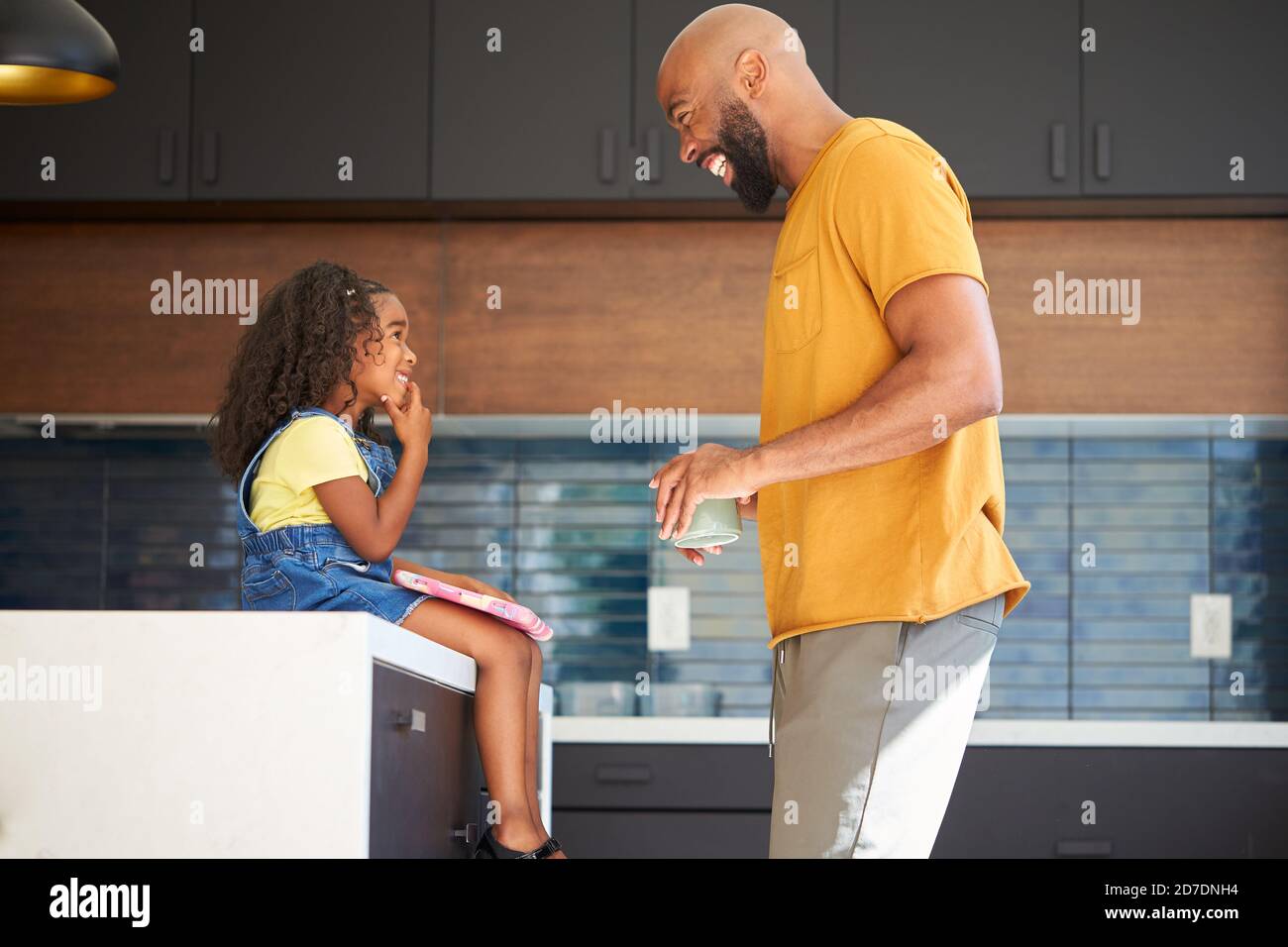 Father With Daughter Sitting On Kitchen Counter At Home Using Digital Tablet Stock Photo