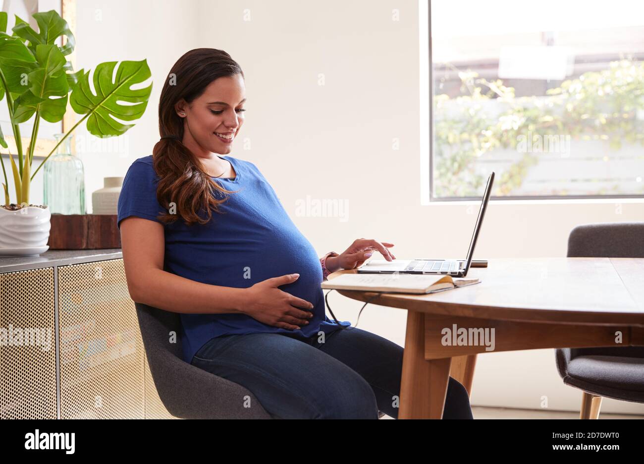 Pregnant Woman Using Laptop At Table Working From Home Stock Photo