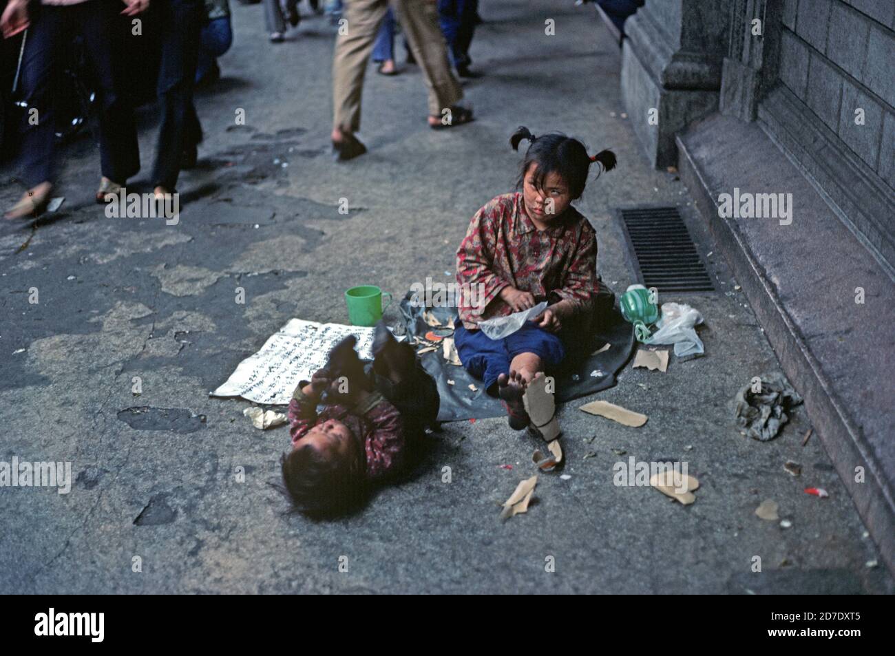 Begging child with eye disability and baby destitute in Chinese street, Nanking, China, 1980s Stock Photo