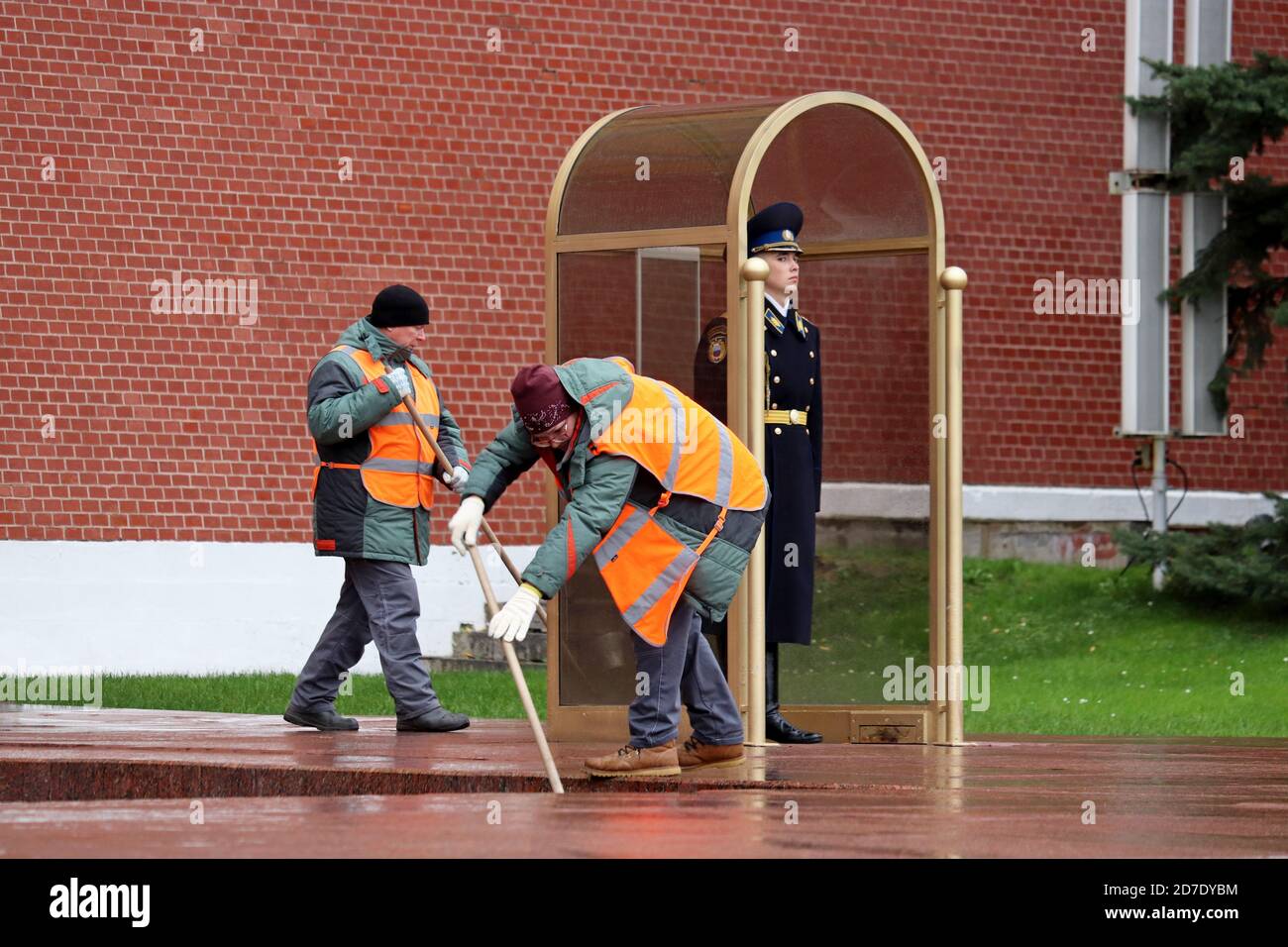 Janitors clean the street near the russian soldier on duty near the Kremlin wall. Street cleaners, the honor guard of the Presidential regiment Stock Photo