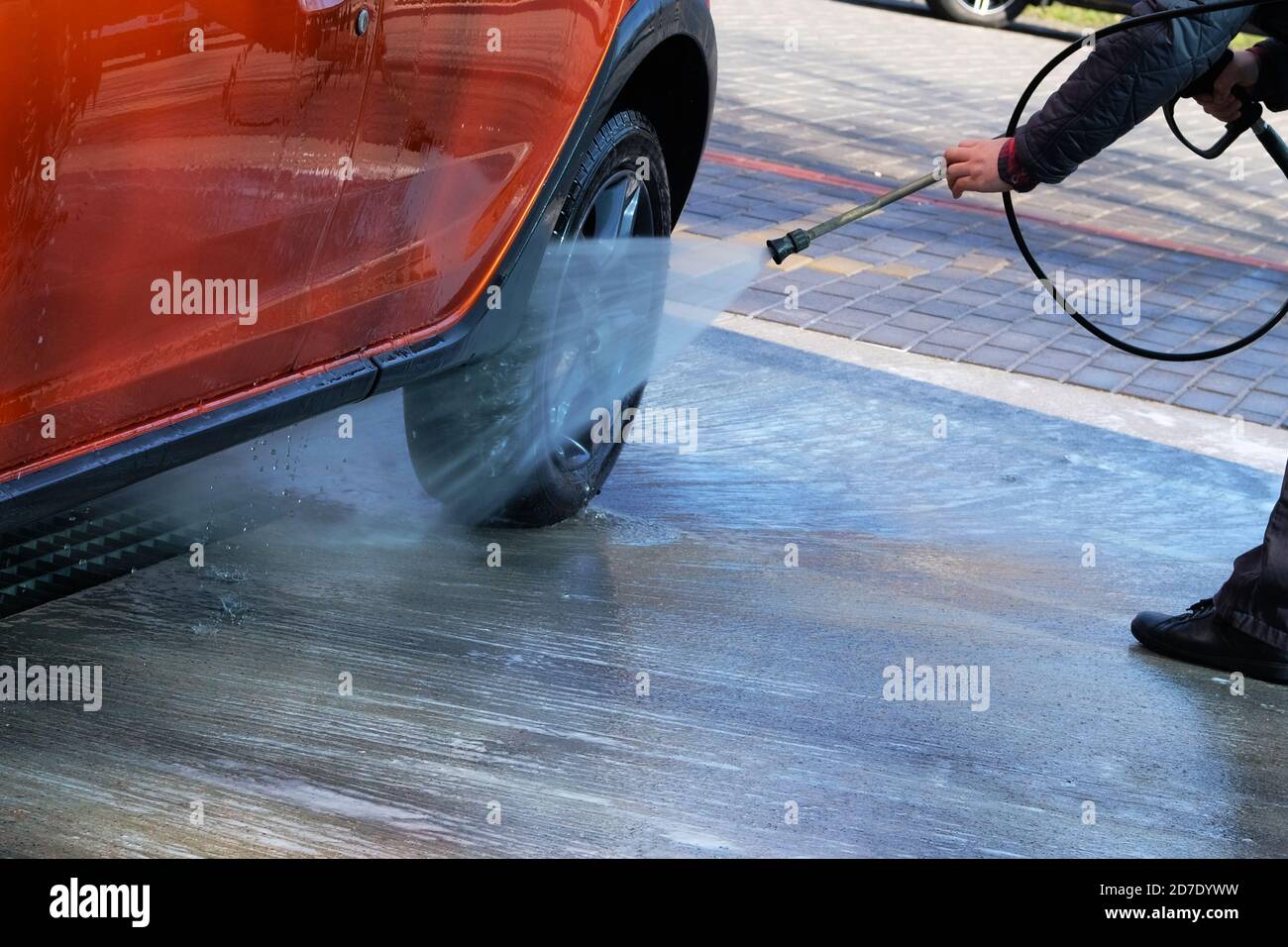 Washing with clean water at self-service car wash. Man washes his orange car at car wash in outdoors. Stock Photo