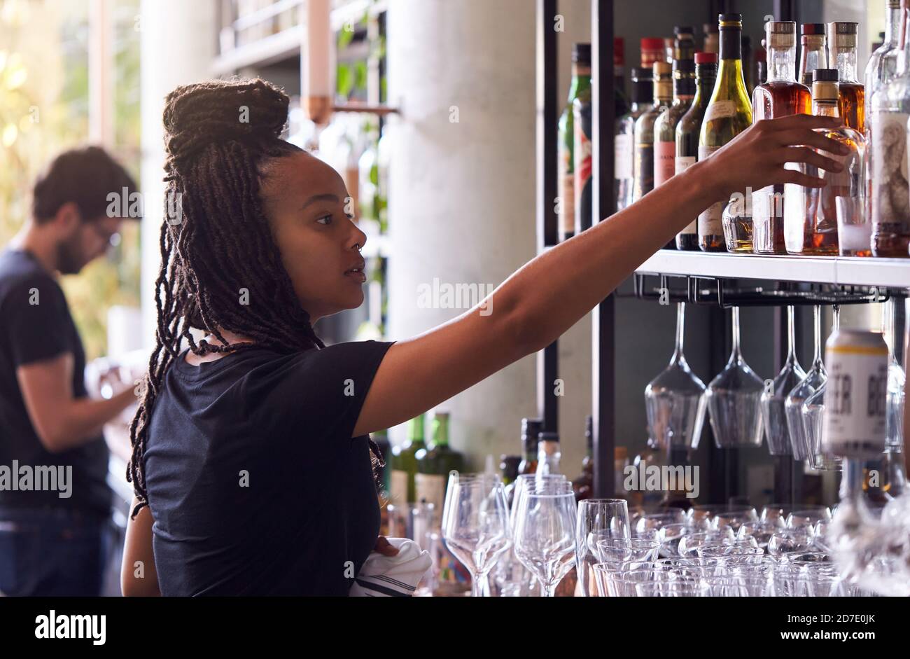 Female Bartender Arranging Bottles Of Alcohol Behind Bar Stock Photo