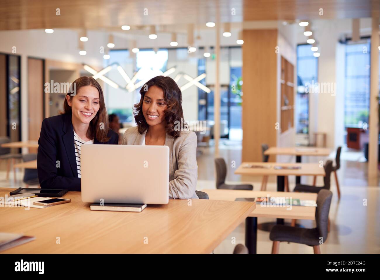 Two Businesswomen With Laptop At Desk In Open Plan Office Collaborating On Project Together Stock Photo