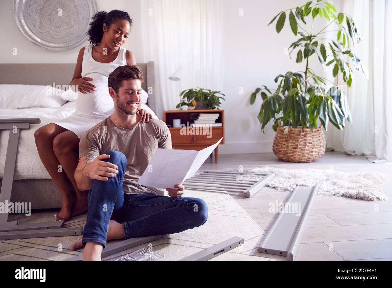 Couple With Pregnant Woman Putting Together Self Assembly Baby Cot In