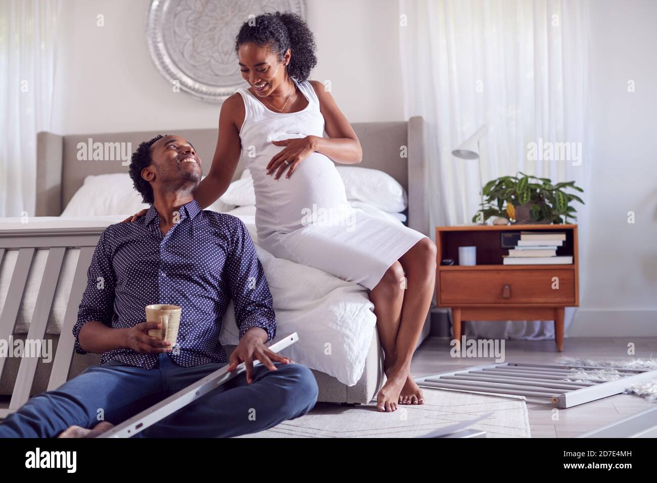 Couple With Pregnant Woman Putting Together Self Assembly Baby Cot In