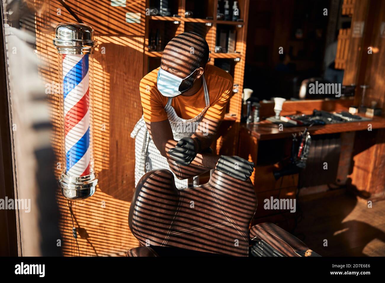 Barber in medical mask leaning on barber chair in Stock