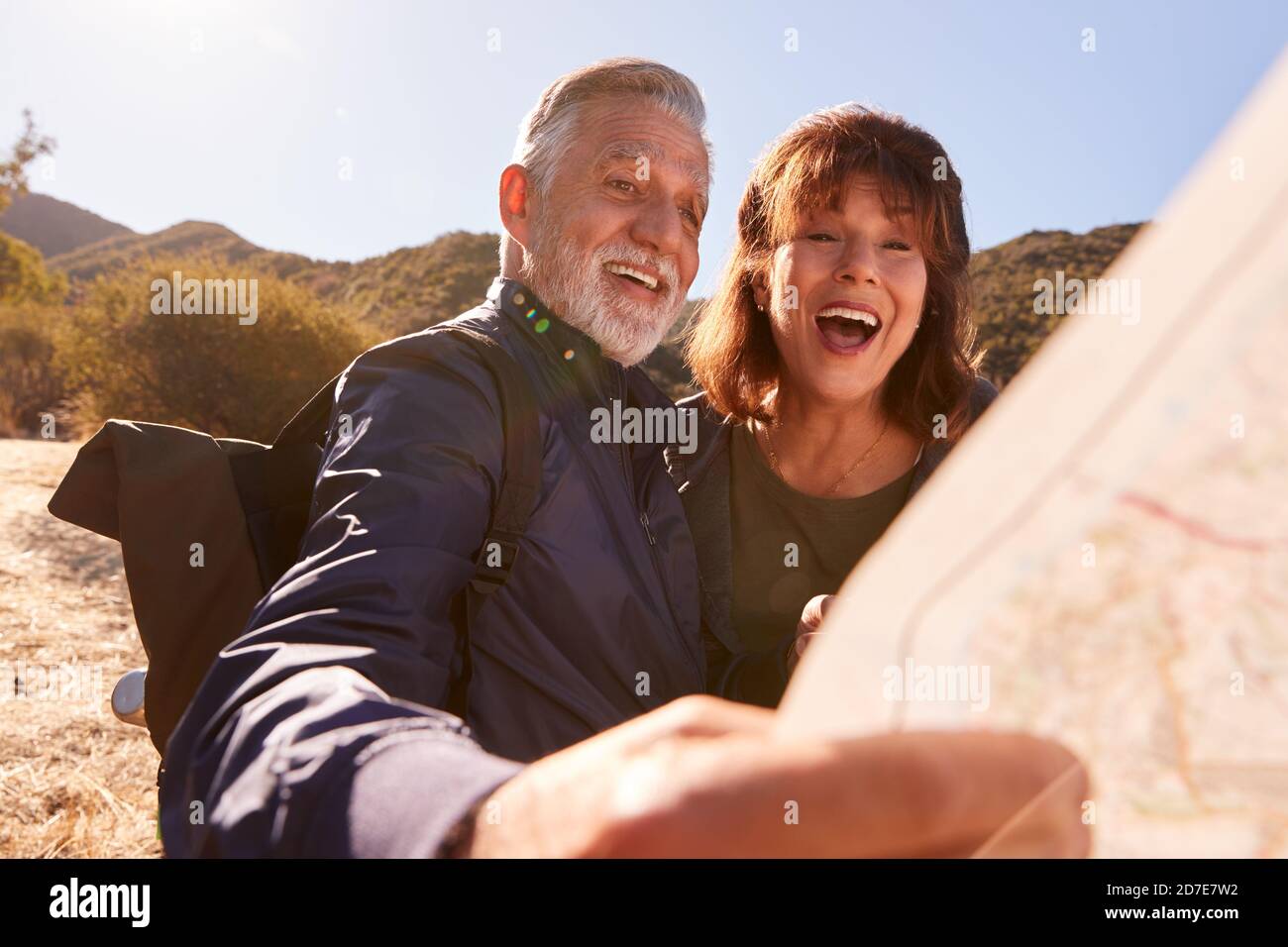 Senior Couple Looking At Map As They Hike Along Trail In Countryside Together Stock Photo