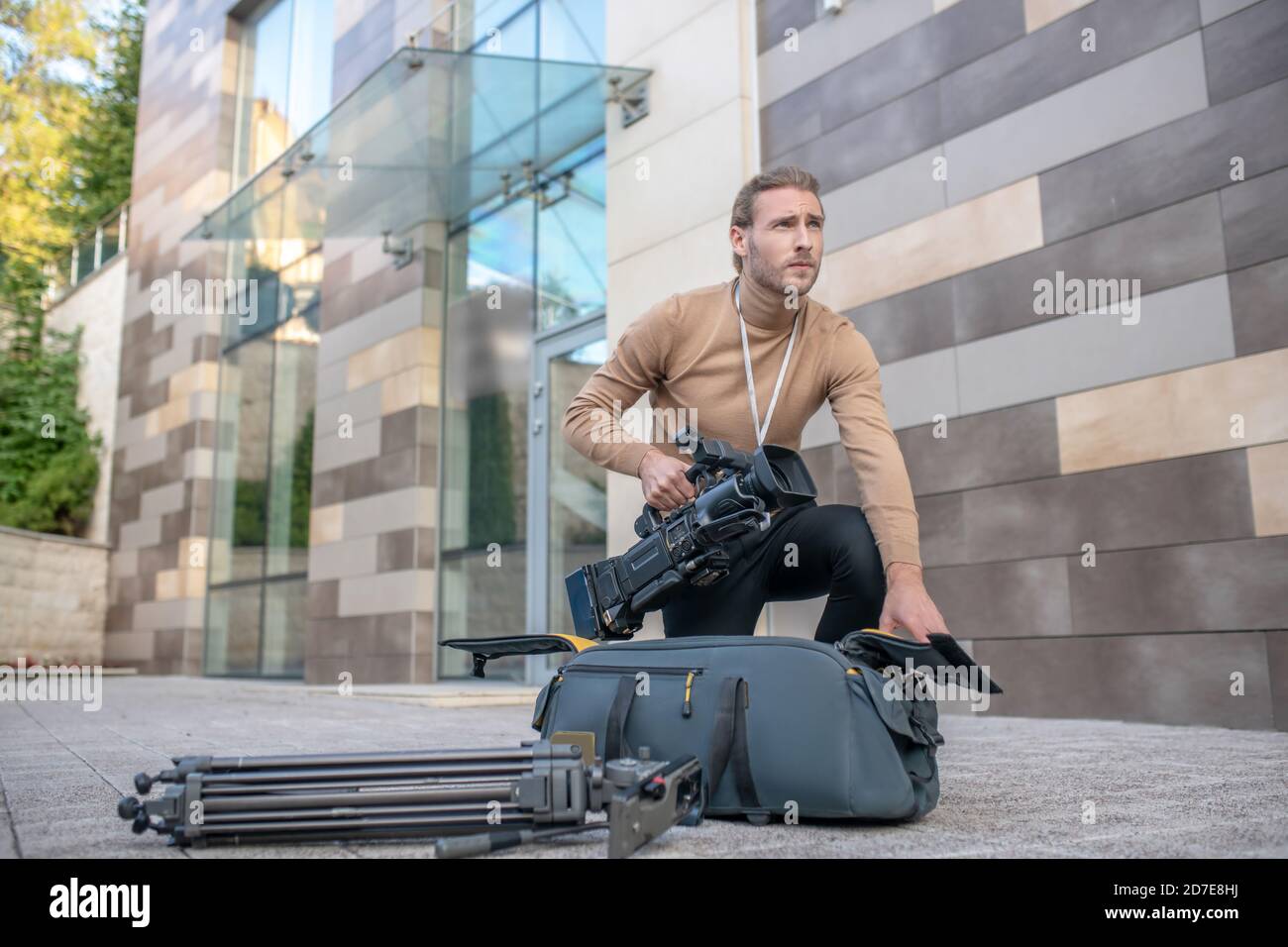 Long-haired cameraman standing on one knee, taking equipment out of case Stock Photo