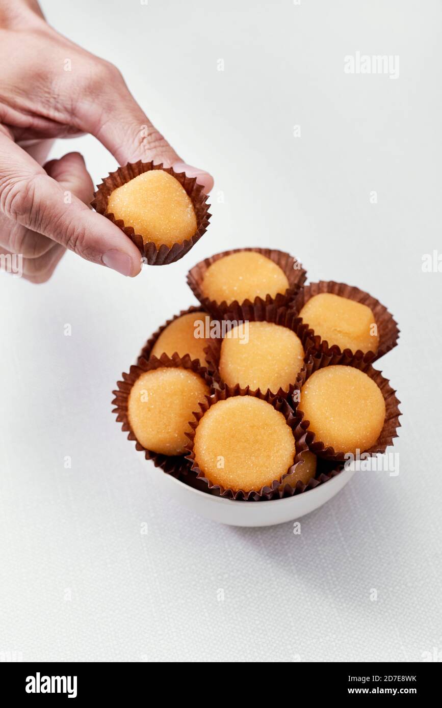 closeup of a man picking one of some yemas de Santa Teresa or yemas de Avila, a confection of Spain, from a bowl on an off-white table Stock Photo -