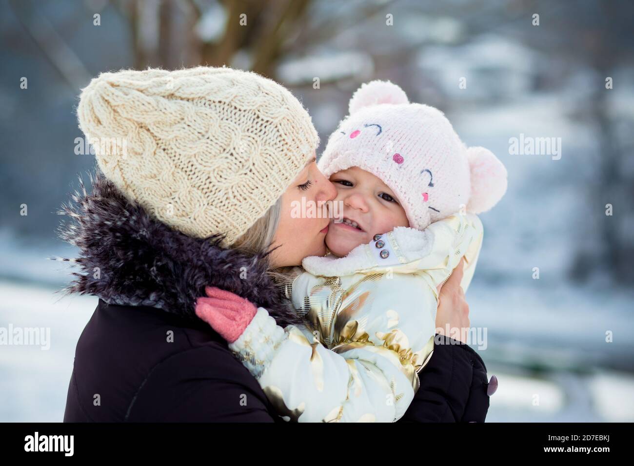 Young mom hugs her little daughter, kisses her on the cheek. Winter time, outdoor activity Stock Photo
