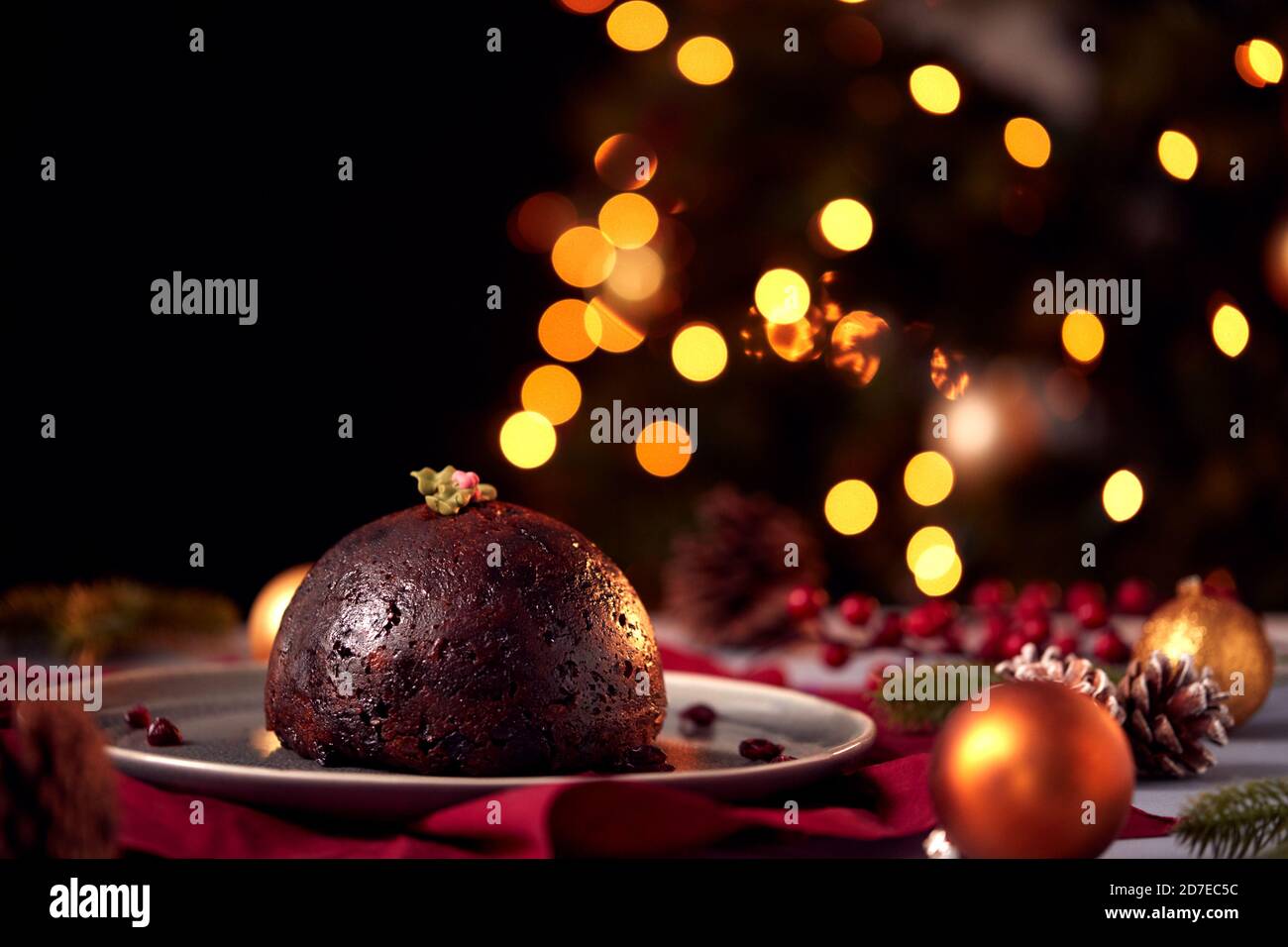 Traditional Christmas Pudding On Table Set For Festive Christmas Meal With Tree Lights In Background Stock Photo