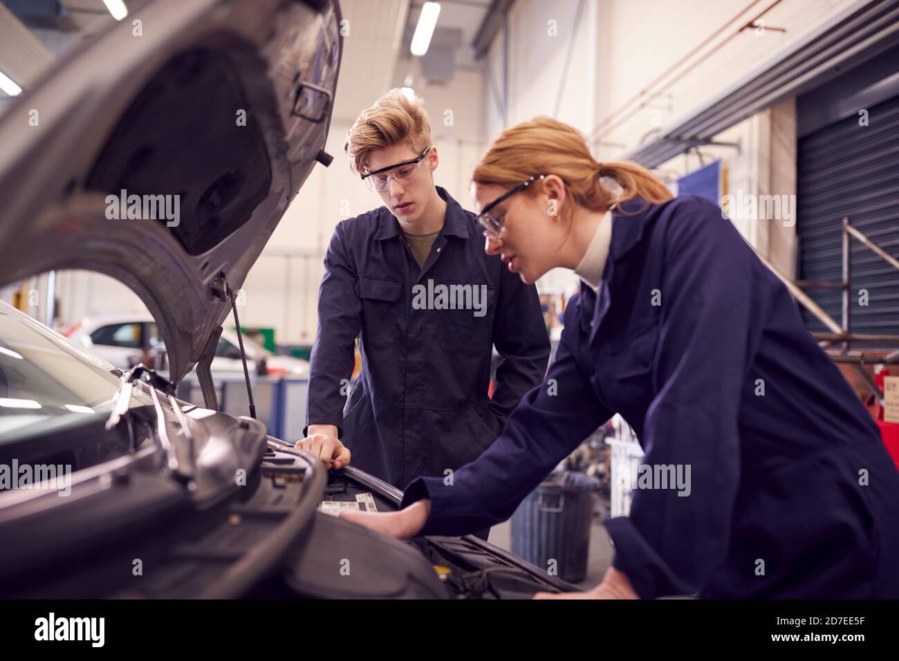 Male And Female Students Looking At Car Engine On Auto Mechanic Apprenticeship Course At College