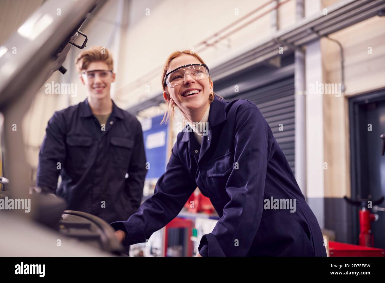 Male And Female Students Looking At Car Engine On Auto Mechanic Apprenticeship Course At College
