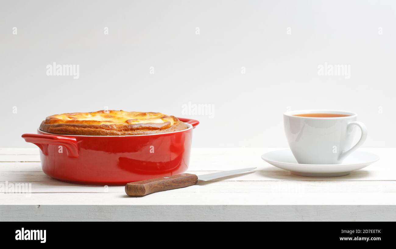 Homemade cottage cheese cheesecake in red ceramic bowl and cup of tea