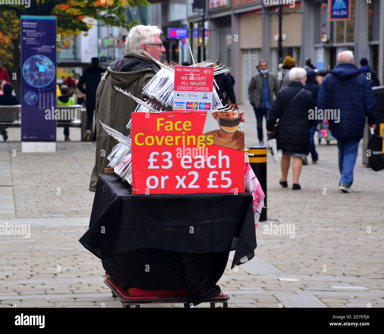 Covid 19 or coronavirus signage and advertising in Manchester, Greater Manchester, England, United Kingdom. A man sells face coverings and masks on Market Street, central Manchester. Stock Photo