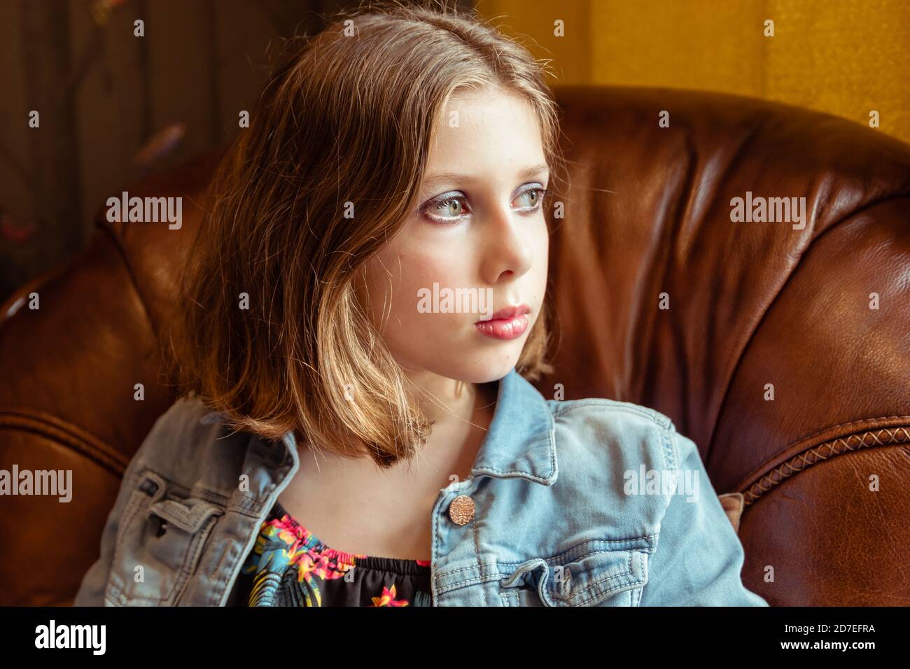 A natural portrait of a tween or teen girl with bobbed hair sat in an armchair, sad or melancholy thoughtfulness Stock Photo