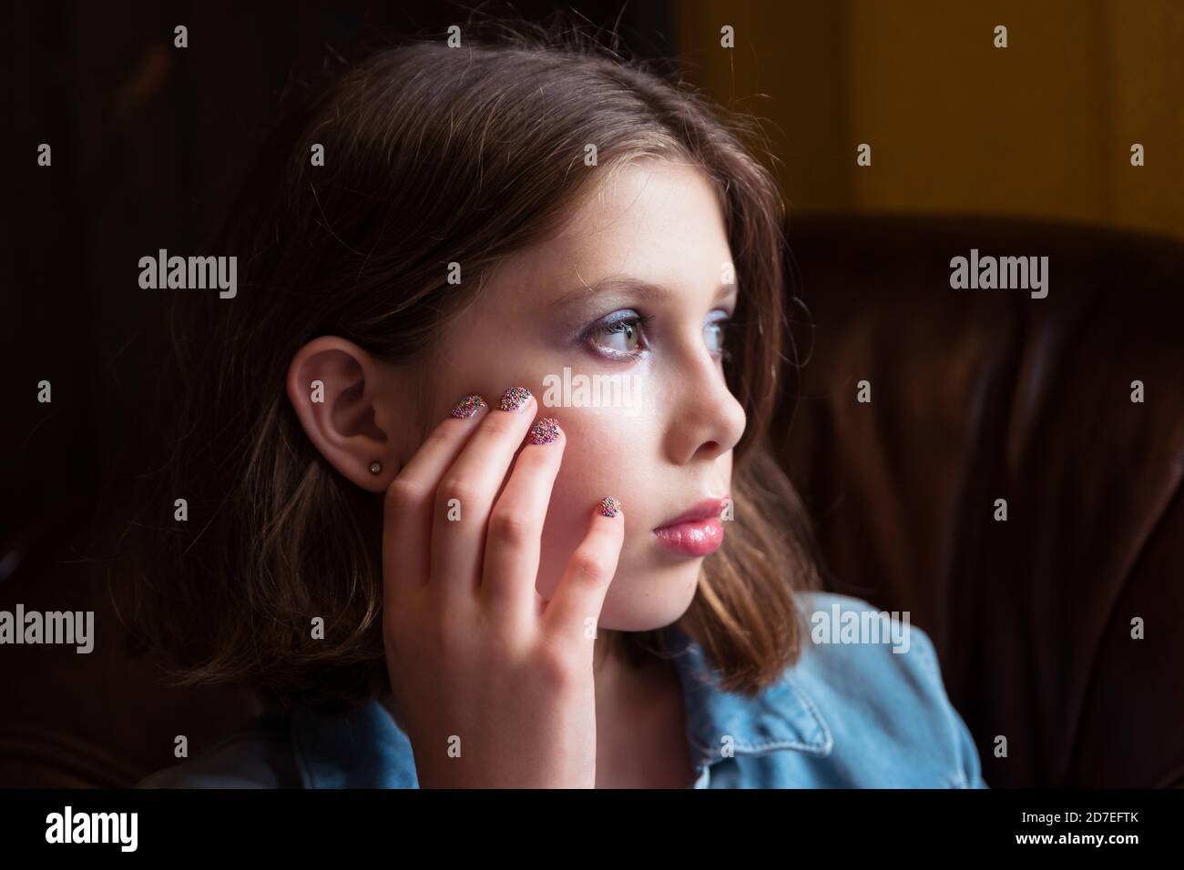 A natural portrait of a tween or teen girl with hand on face sat in an armchair, looking contemplative Stock Photo