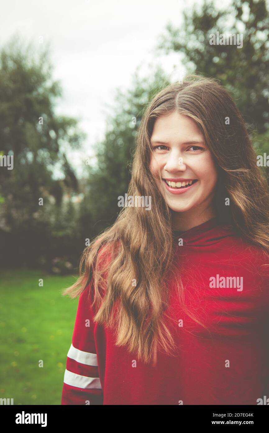 Beautiful natural portrait of teenage girl with long brown hair looking at camera with smile showing teeth Stock Photo