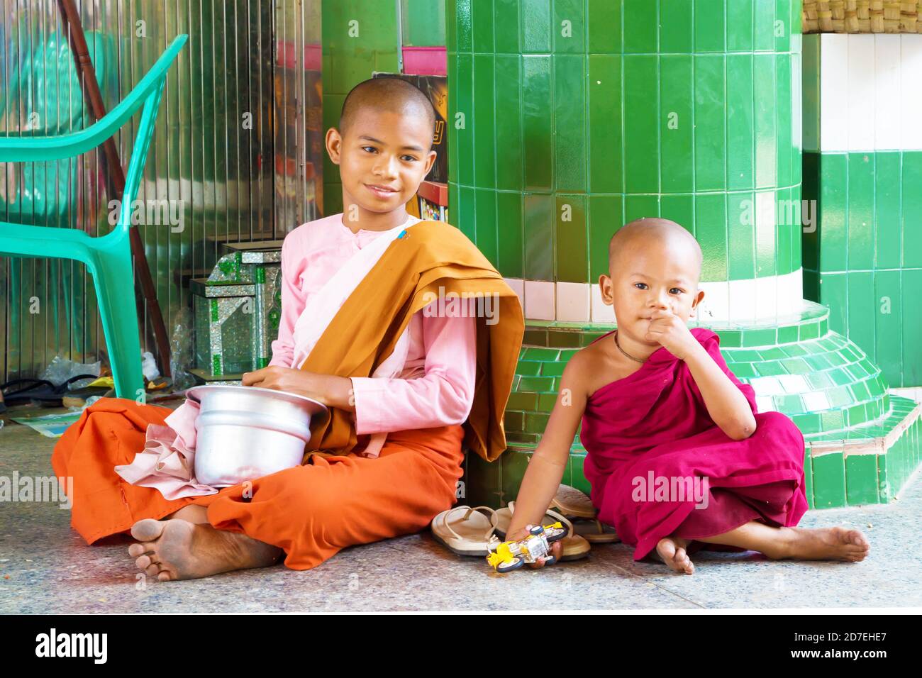 Elder girl and child dressed as buddhist nun and monk. They are sitting close to the column of a temple. Stock Photo