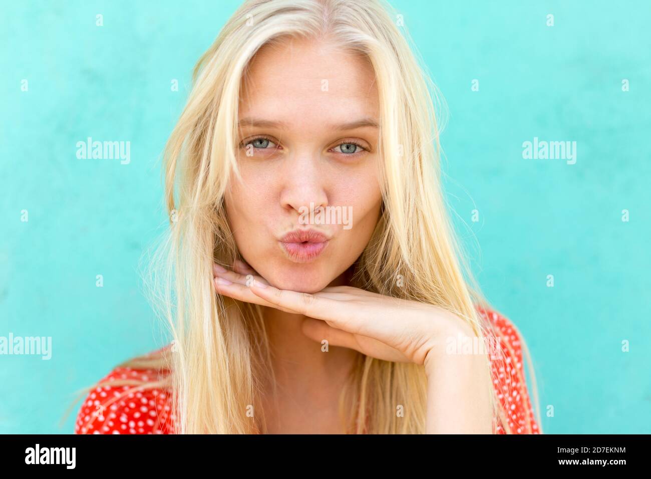 Portrait of beautiful young blonde woman giving a kiss and posing to the camera isolated against a turquoise background. Stock Photo
