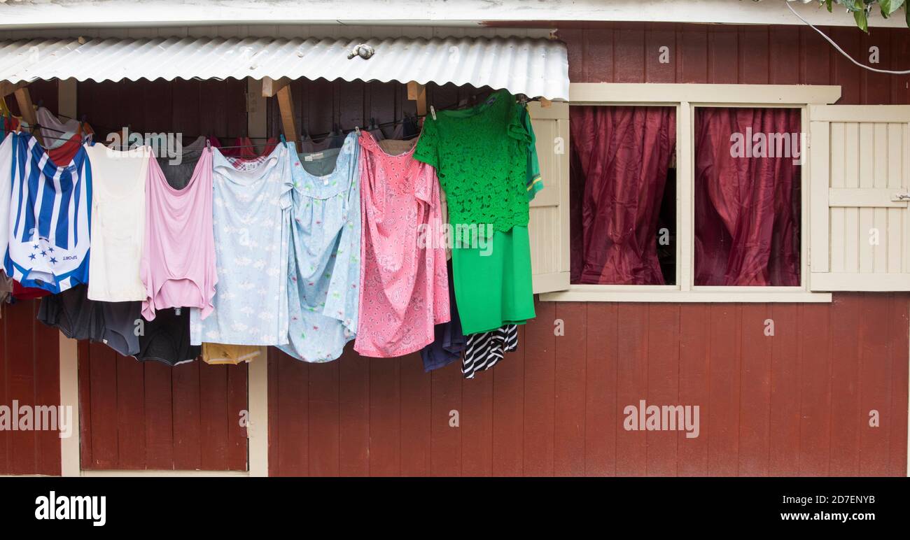 Colorful clothing dries on a line against a red wall in Roatan, Honduras. Stock Photo