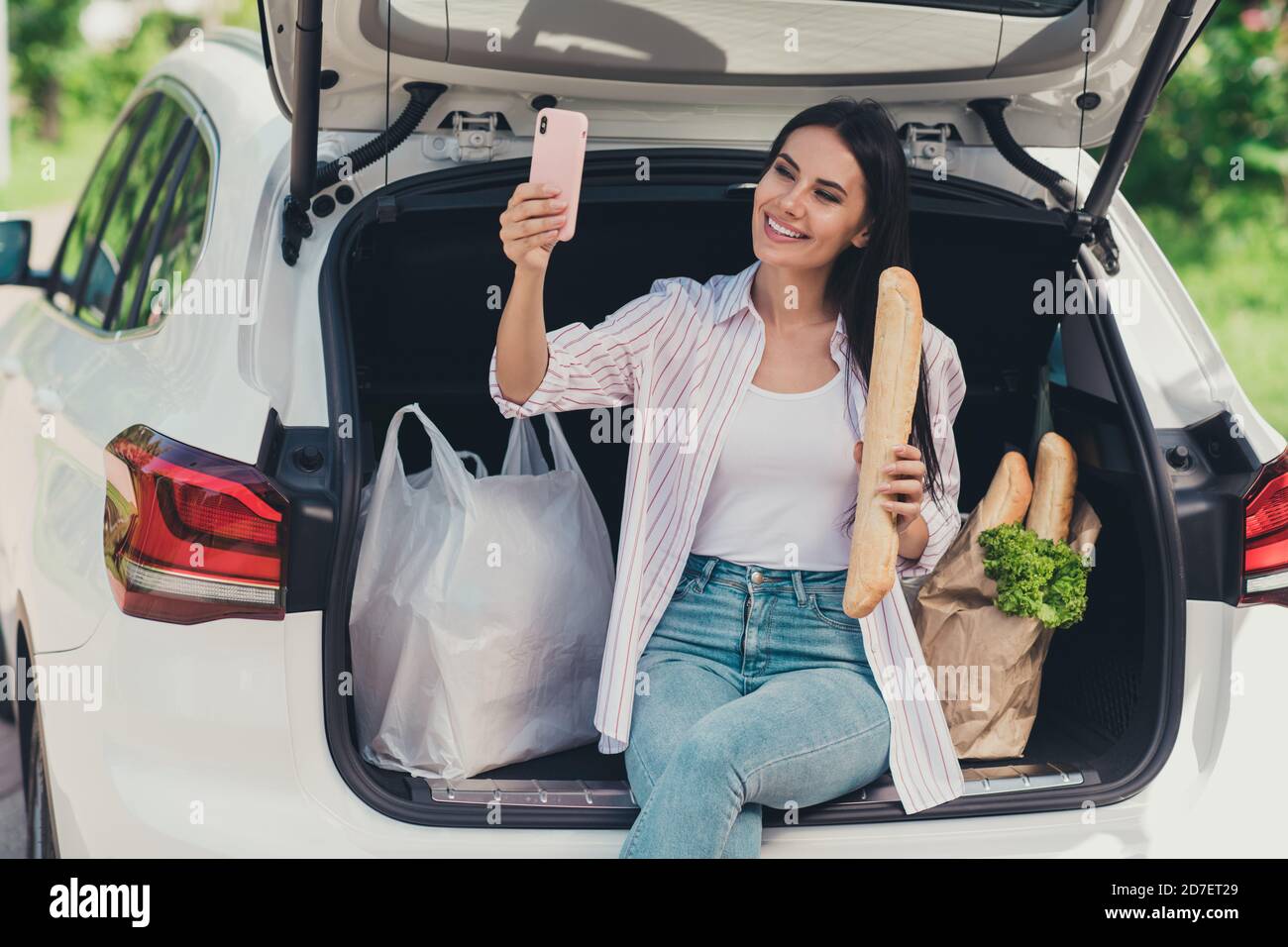 Portrait of her she nice attractive cheerful cheery lady blogger sitting in trunk carrying fresh bread ingredients bio farm products baguette supply Stock Photo