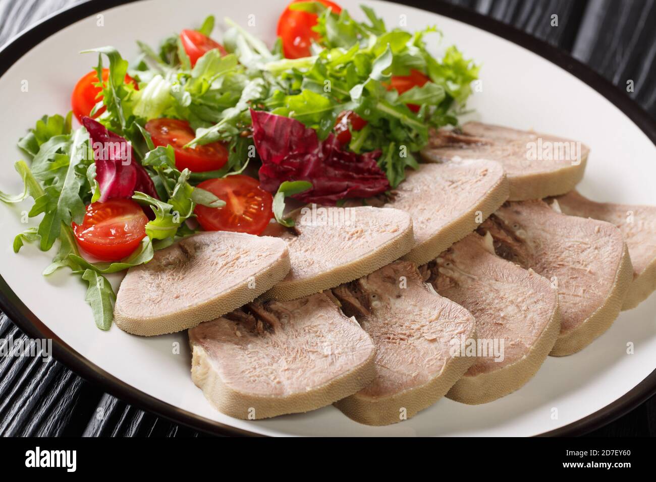 Serving of boiled beef tongue with fresh salad close-up in a plate on the table. horizontal Stock Photo