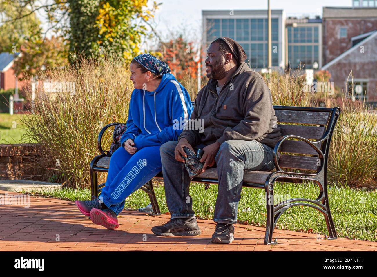 Frederick, MD, USA 10/14/2020: An interracial couple (caucasian woman and African American man) are sitting together on a park bench. The woman wears Stock Photo