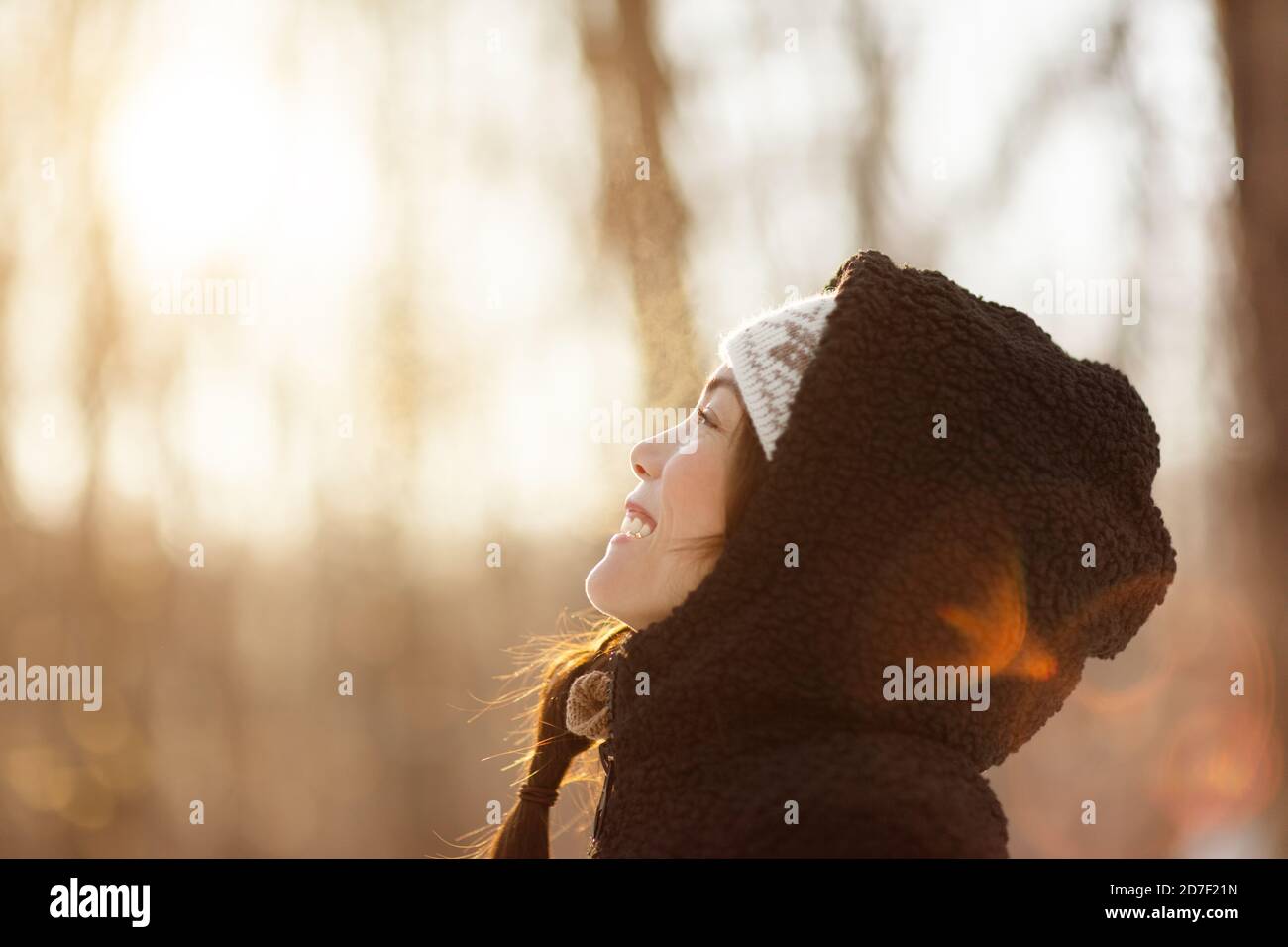 Winter happy woman breathing cold air outside young people lifestyle. Asian girl looking up at snow falling in forest wearing hooded jacket Stock Photo
