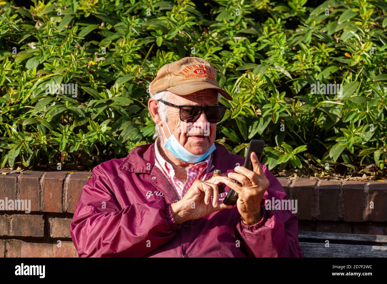 Frederick, MD, USA 10/14/2020: An elderly caucasian man is trying to dial a number on the keyboard of his old flip phone while holding a cigar between Stock Photo