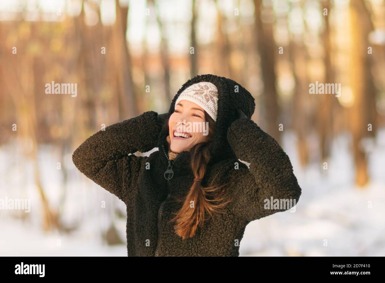Winter snow fun happy girl walking outside in cold weather protecting ears holding wool hat over ears active outdoor lifestyle. Asian girl wearing Stock Photo