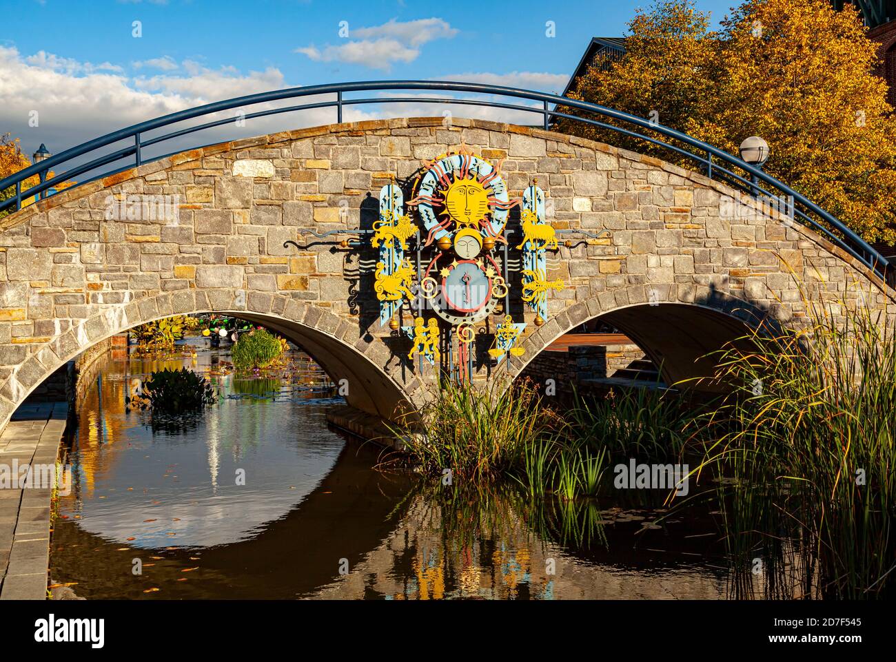 Frederick, MD, USA 10/13/2020: A scenic stone arched bridge on Carroll Creek with zodiac themed metal art decorations on it. Autumn leaves fall on wat Stock Photo