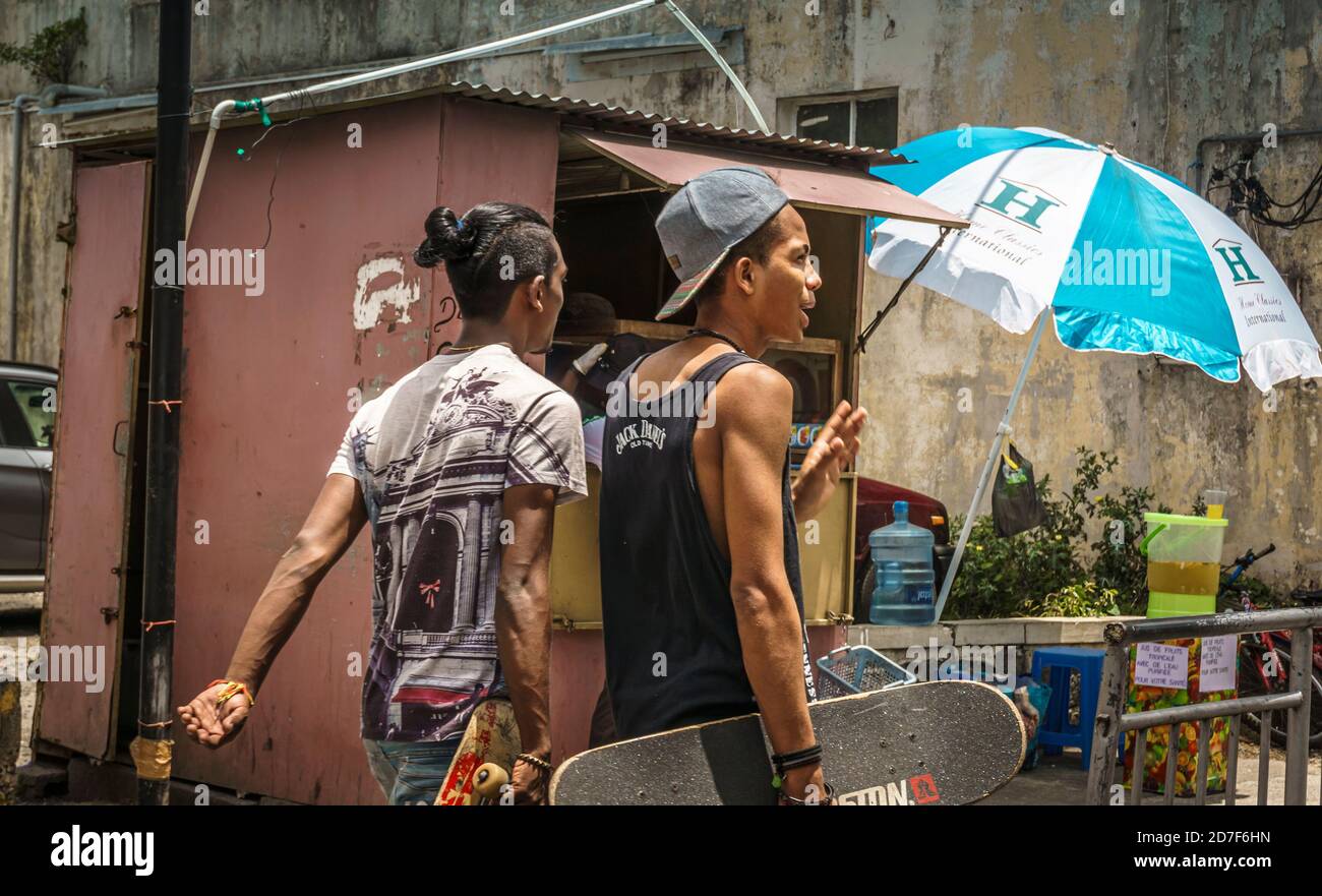 Mauritius, December 2015 - Two young men of African ethnicity carry their skateboards while walking and talking  Stock Photo