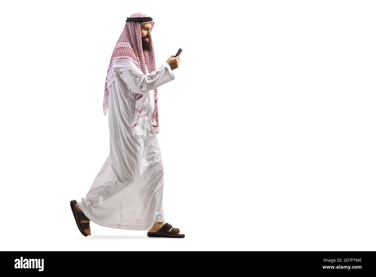 Full length profile shot of an arab man using a smartphone and walking isolated on white background Stock Photo