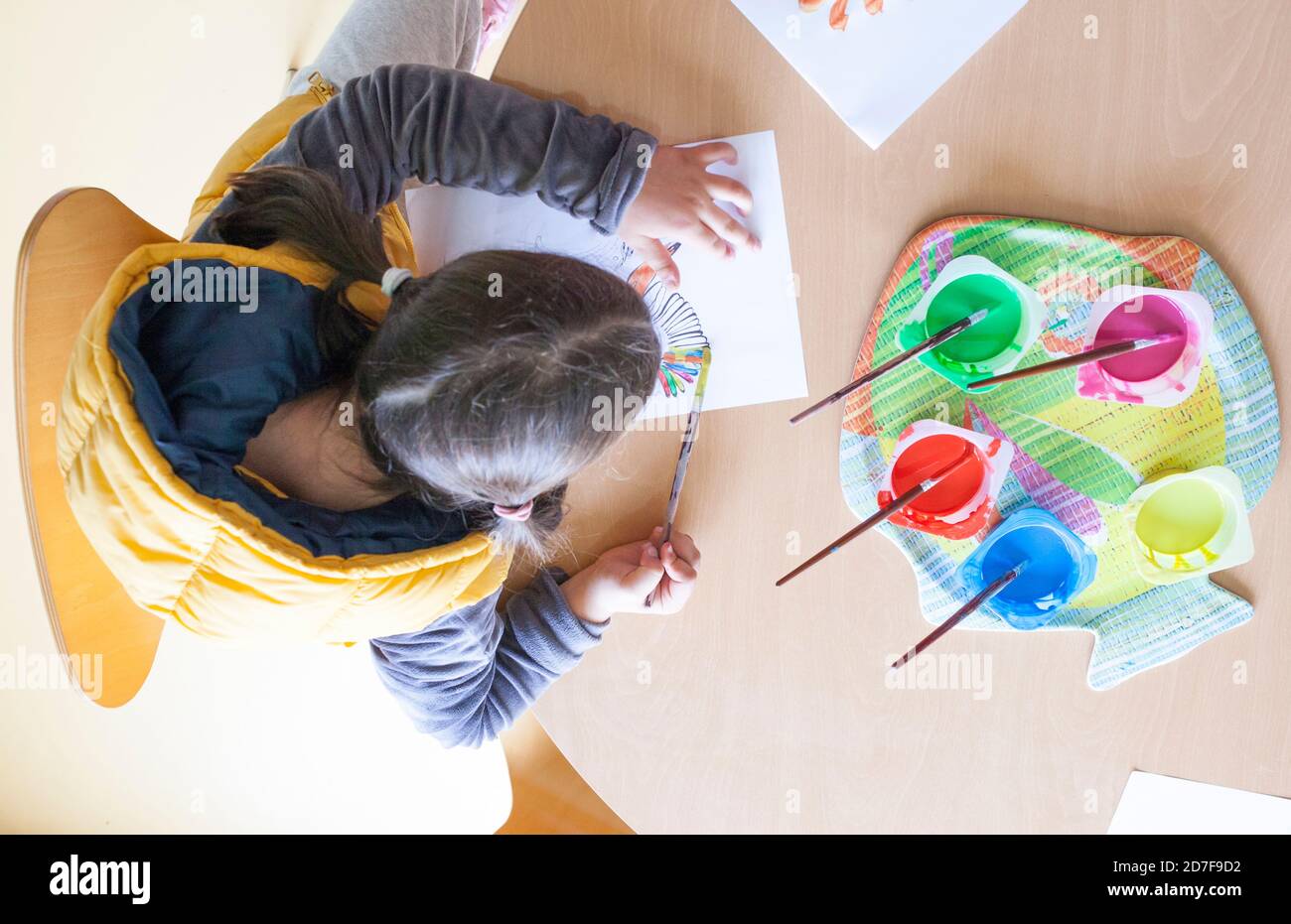 Child girl painting with sashable Tempera paint. Yogurt cups reused as