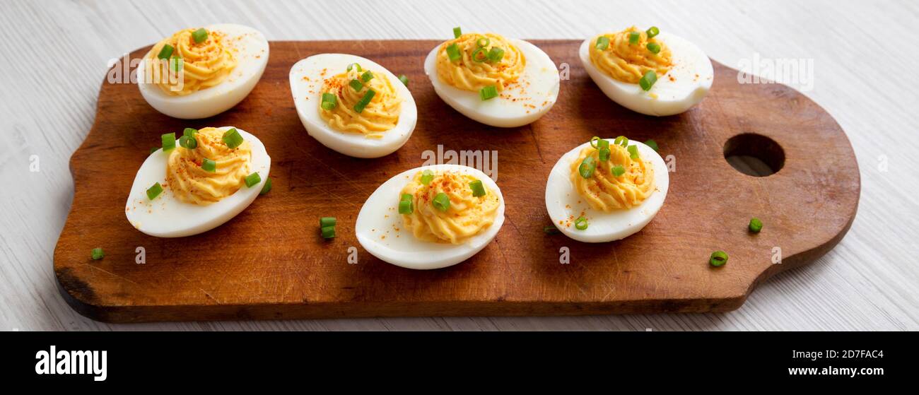 Homemade Deviled Eggs with Chives on a rustic wooden board on a white