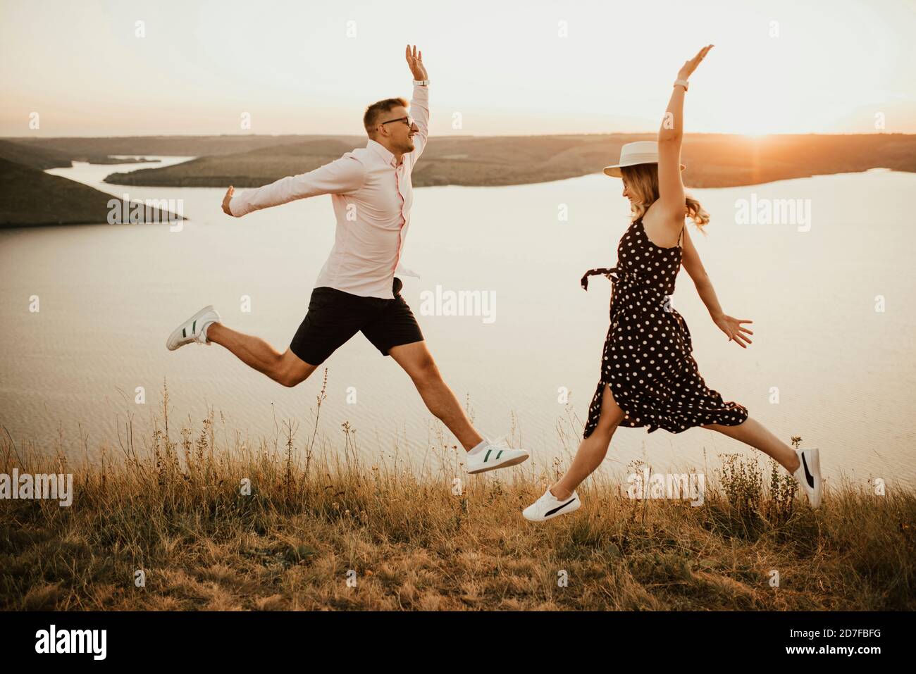 man and woman in love jumping on mountain above large lake by the sea at sunset Stock Photo