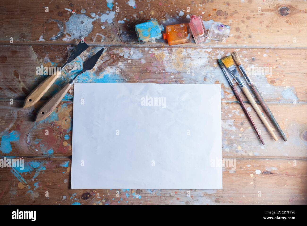 Artists desk and materials mockup.Various brushes and pallete knives.The image contains one blank white sheet of paper ideal for a creative mockup. Stock Photo