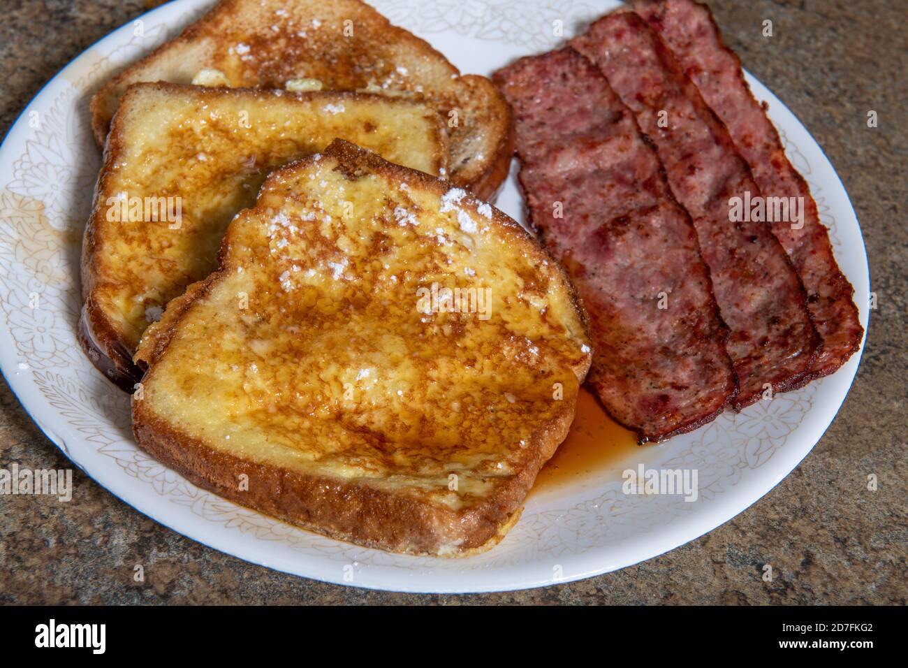 A plate of French toast that has powdered sugar and maple syrup on it