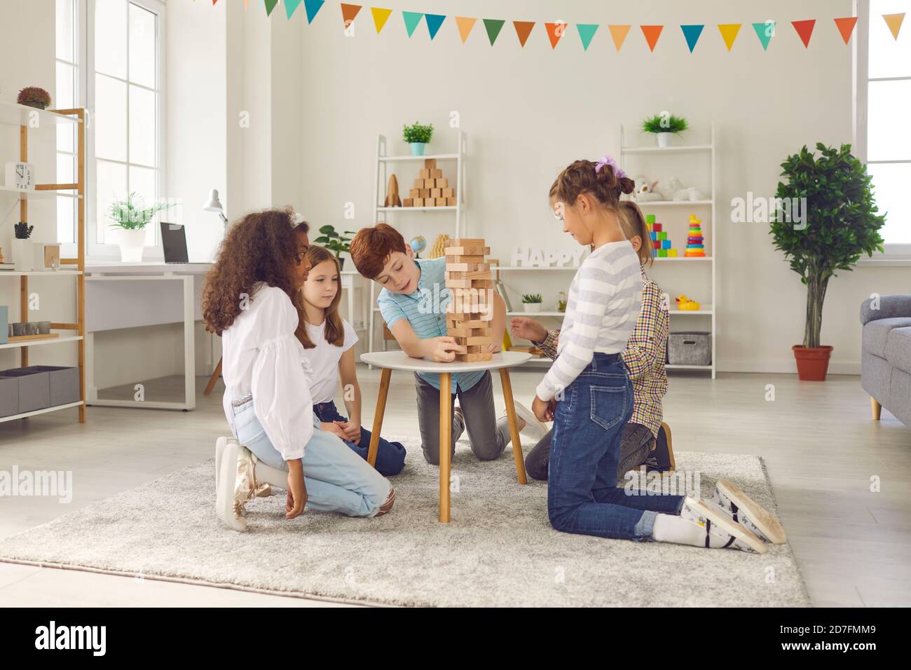 Group of diverse children sitting on floor and playing board game with wooden blocks at home. Stock Photo