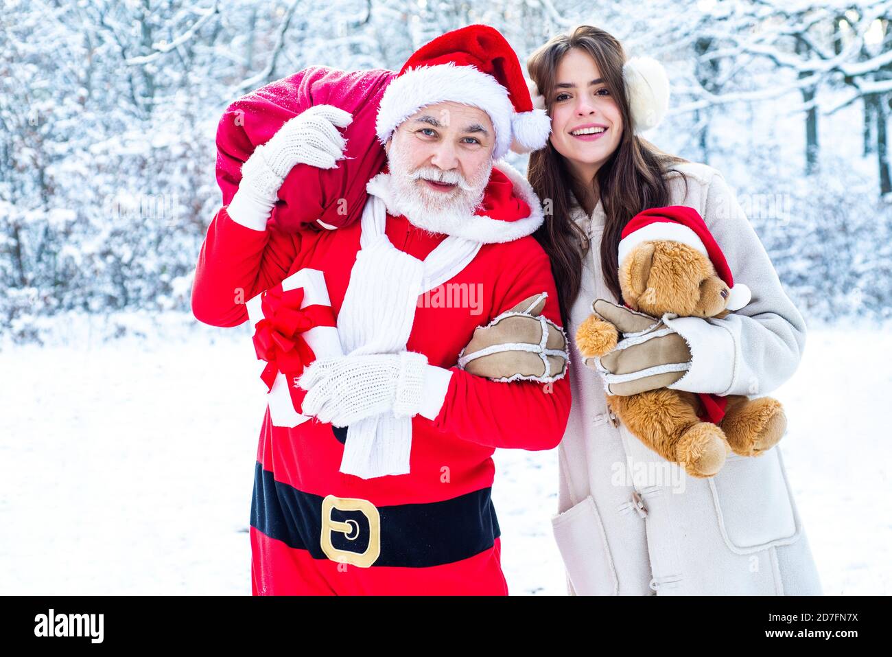 Santa with winter girl in red suit walking along the road to Christmas. Santa Claus and snow girl in red costume walk in winter forest. Stock Photo
