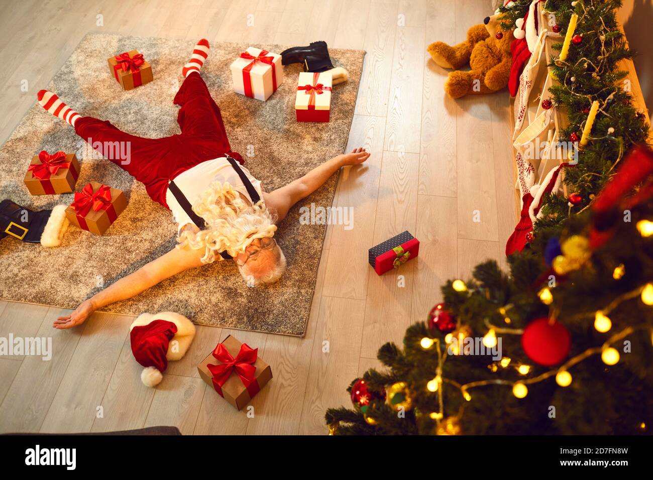 Drunk or simply tired Santa Claus sleeping on floor of a living-room with presents scattered around Stock Photo