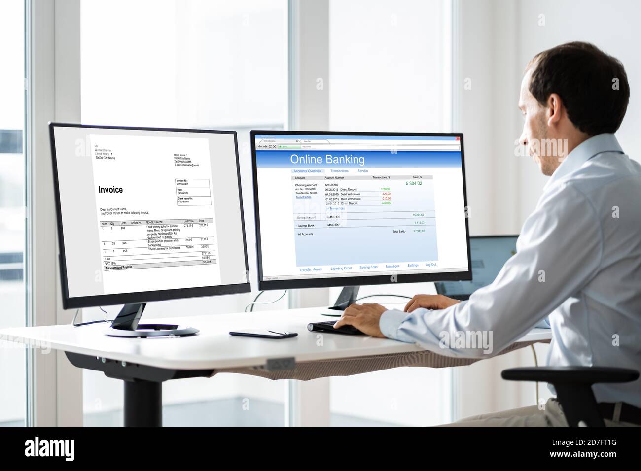 Young Businessman Looking At Invoice While Doing Online Banking On Computer Stock Photo