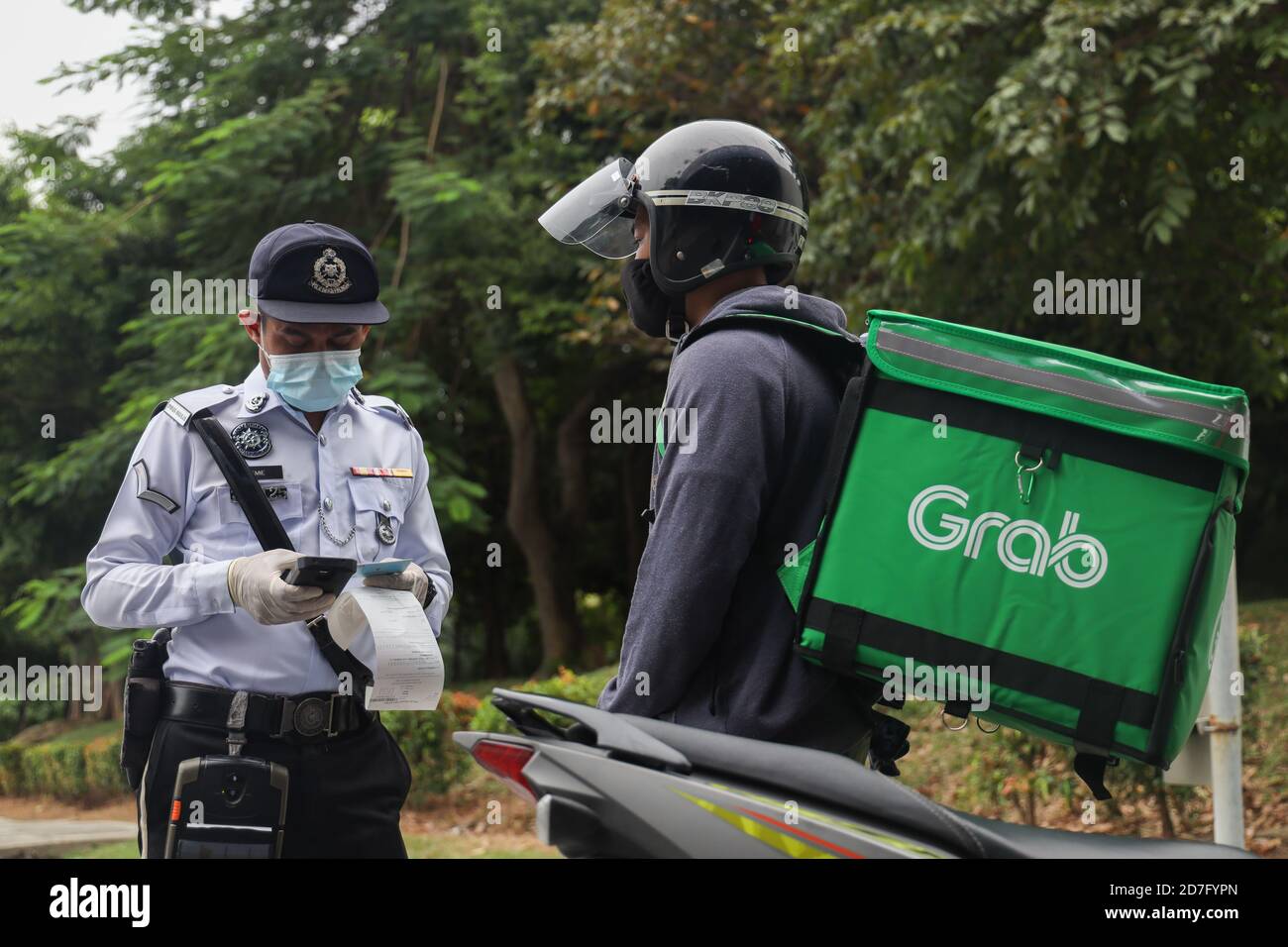 A police officer wearing a face mask questions a Grab deliver to ensure he abides to the requirement of the Conditional Movement Control Order (CMCO) in Selangor state, Putrajaya and Kuala Lumpur as cases spike amid concerns of the coronavirus (Covid-19). Stock Photo