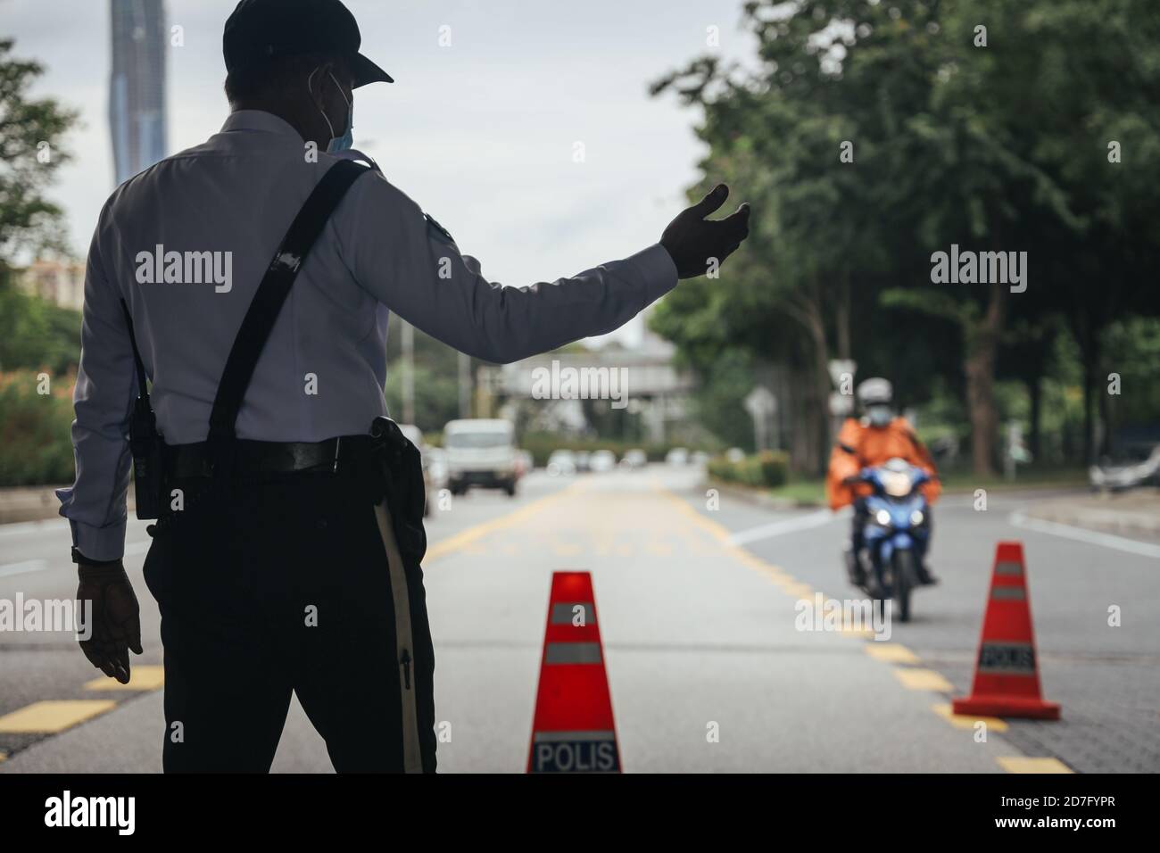 A police officer makes a hand gesture to an incoming vehicle during a roadblock to ensure the citizen abide to the requirement of the Conditional Movement Control Order (CMCO) in Selangor state, Putrajaya and Kuala Lumpur as cases spike amid concerns of the coronavirus (Covid-19). Stock Photo
