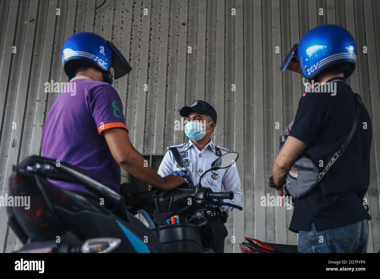 A police officer wearing face masks checks motorcyclists during a roadblock to ensure the citizens abide to the requirement of the Conditional Movement Control Order (CMCO) in Selangor state, Putrajaya and Kuala Lumpur as cases spike amid concerns of the coronavirus (Covid-19). Stock Photo