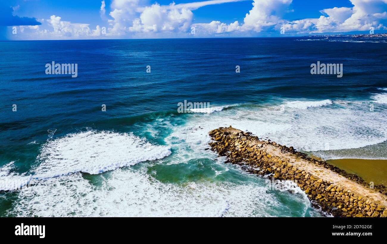 Aerial view or drone photo of rocky pier or breakwater in the blue ocean. Costa Da Caparica, Setubal, Almada, Portugal Stock Photo