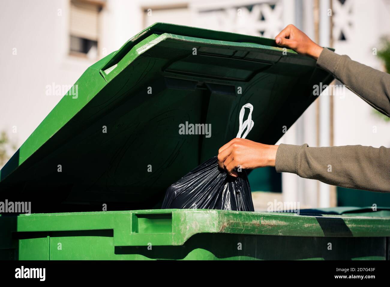 Man throwing out black eco-friendly recyclable trash bag in to big plastic green garbage container. Take out the trash Stock Photo