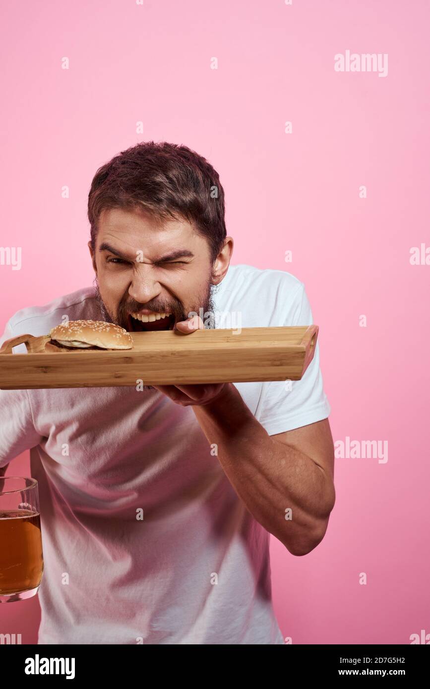 Aggressive guy with a tray in his hands hamburger fries pink background ...
