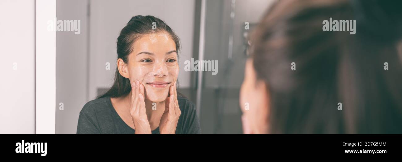 Face wash young Asian woman applying scrub exfoliating skin in beauty skincare routing morning lifestyle - Bathroom mirror panoramic banner panorama Stock Photo